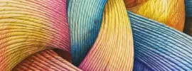 A close-up of colorful, intricately woven threads forming a harmonious and complex pattern. The fibers, in shades of pink, yellow, blue, and purple, intertwine seamlessly, showcasing texture and depth under soft lighting.